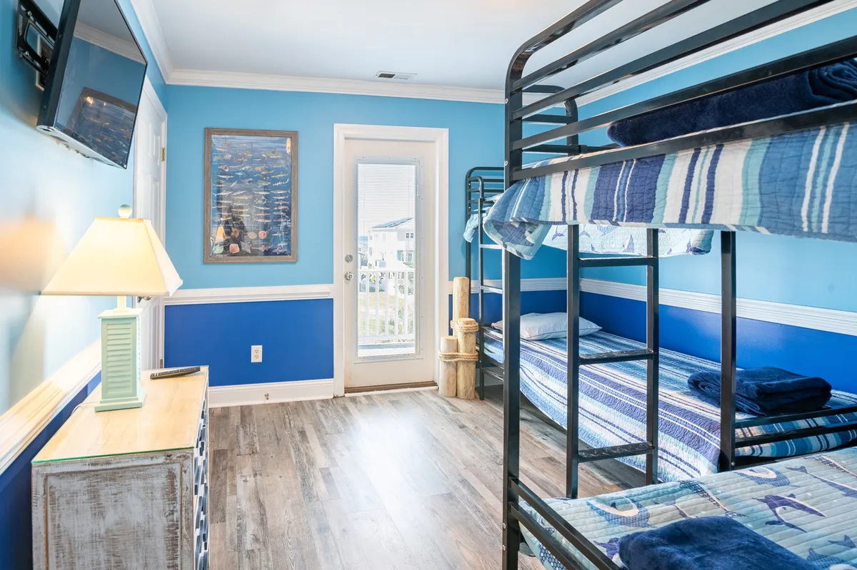 A playful bunk room featuring bunk beds with a blue accent wall and a cheerful lampshade. The atmosphere is relaxed and fun, perfectly suited for kids or flexible sleeping arrangements.