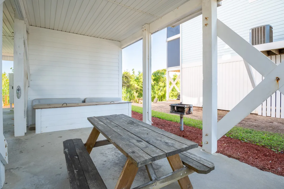 A relaxed grill and picnic area featuring a wooden picnic table, built-in bench seating, a grill, and lush greenery in the background. The space is perfect for outdoor dining, barbecues, and family gatherings.