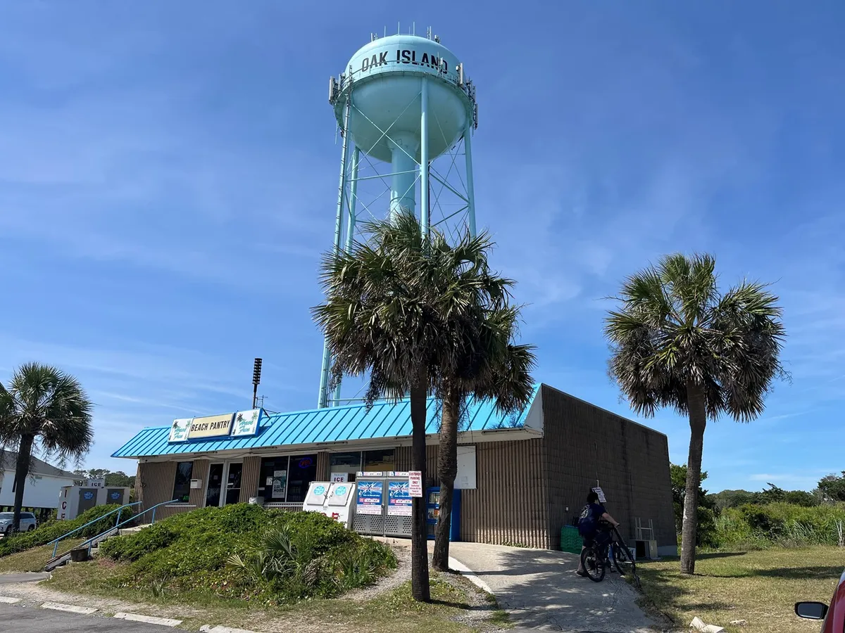 This exterior image features a welcoming scene with a local water tower, palm trees, and an entrance sign, evoking the laid-back seaside atmosphere and hinting at the proximity to local attractions and the beach.