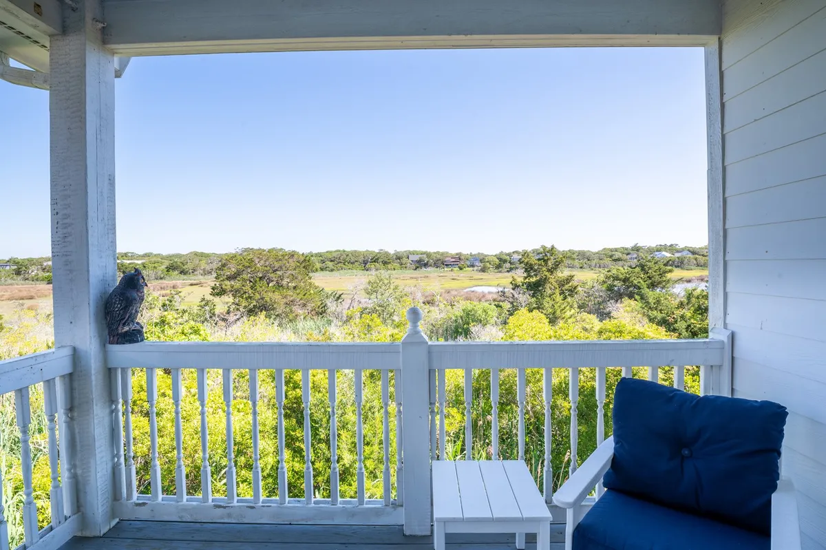 A cozy ocean-view porch with white railings, a blue chair, and a small table, framed by lush greenery. The porch offers a tranquil setting perfect for relaxing after a day of beach adventures.