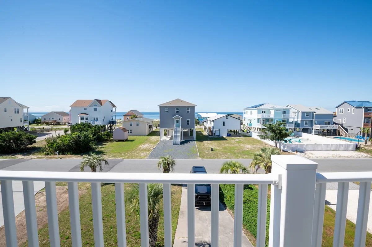 A stunning view from a balcony, featuring palm trees, a manicured lawn, and the sparkling ocean beyond. The vantage point is ideal for watching sunrises, catching evening breezes, and gathering with friends or family against a backdrop of classic coastal beauty.