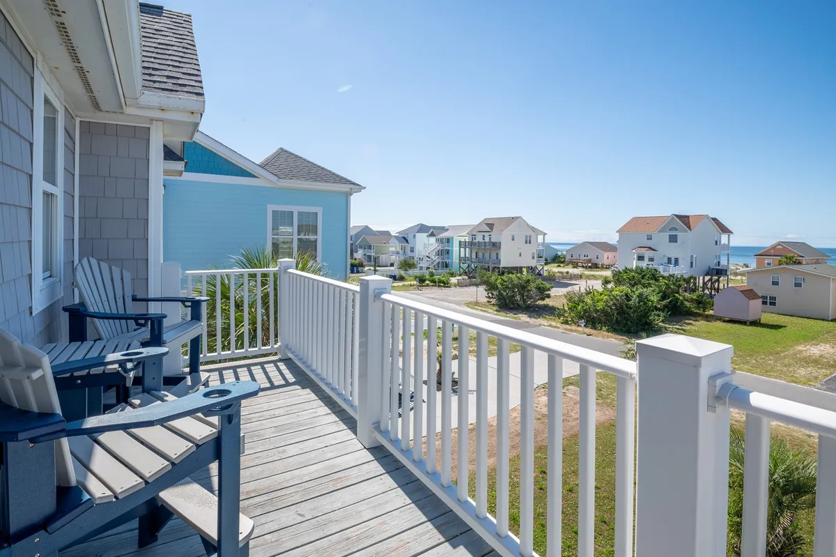 A serene view from a balcony or porch, with adirondack chairs positioned to enjoy the sweeping vistas of nearby houses and the surrounding landscape. The scene is peaceful, ideal for quiet reflection or spending time with loved ones amidst coastal beauty.