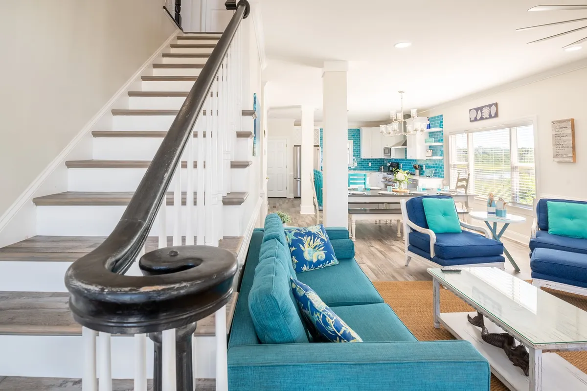 This image captures a blue couch in the foreground with a visible kitchen area and a staircase, suggesting an open and welcoming space for gatherings and easy access to home amenities before heading out for an island adventure.