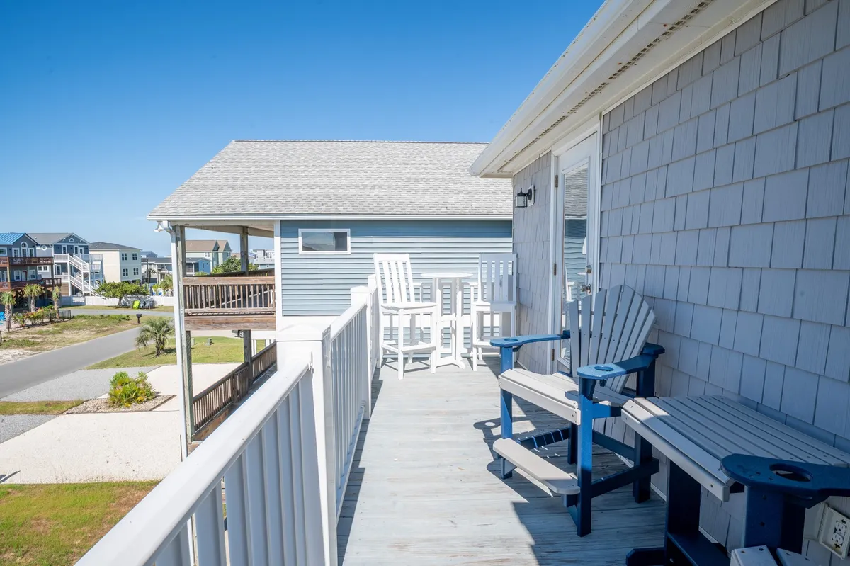 A serene deck with white patio chairs and a blue Adirondack chair overlooks the outdoor area, framed by the sturdy deck railing. The arrangement encourages group conversation and socializing, while the open-air setting invites guests to enjoy morning sunrises or evening gatherings under the stars.