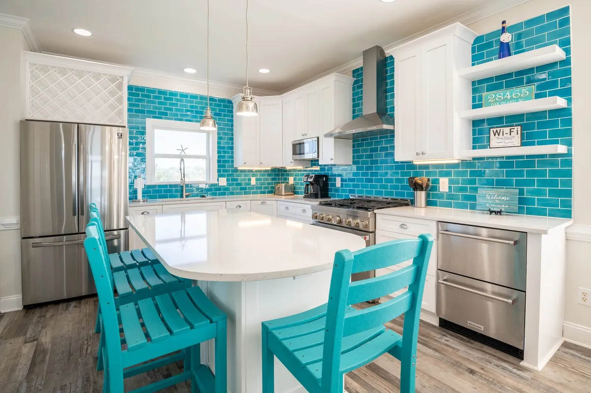 A bright, stylish kitchen featuring a turquoise backsplash, sleek white countertops, stainless steel appliances, and inviting bar stools—showcasing a space designed for both gourmet cooking and socializing.
