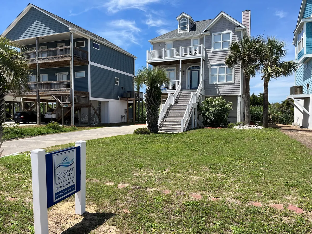 This image shows the large beach house framed by lush palm trees and a visible rental sign, suggesting a welcoming environment perfect for group gatherings. The exterior setting implies ample space for outdoor activities and social events, and the inviting porch is an ideal spot for sharing meals or relaxing together.